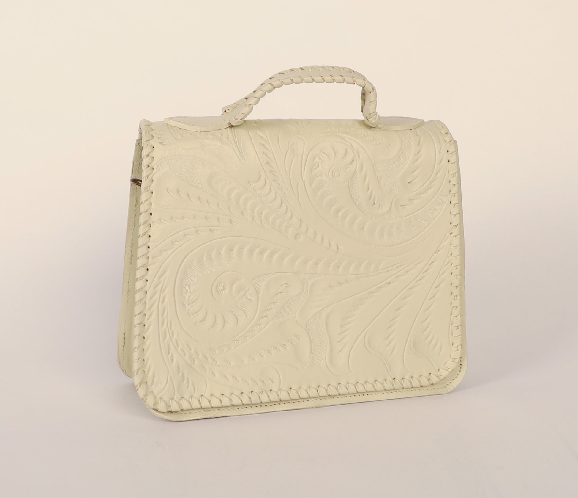 Medium-sized authentic leather handbag with a traditional mexican etching design on the upper flap. Braided handle on top. Fully lined with suede. Front view in color white.