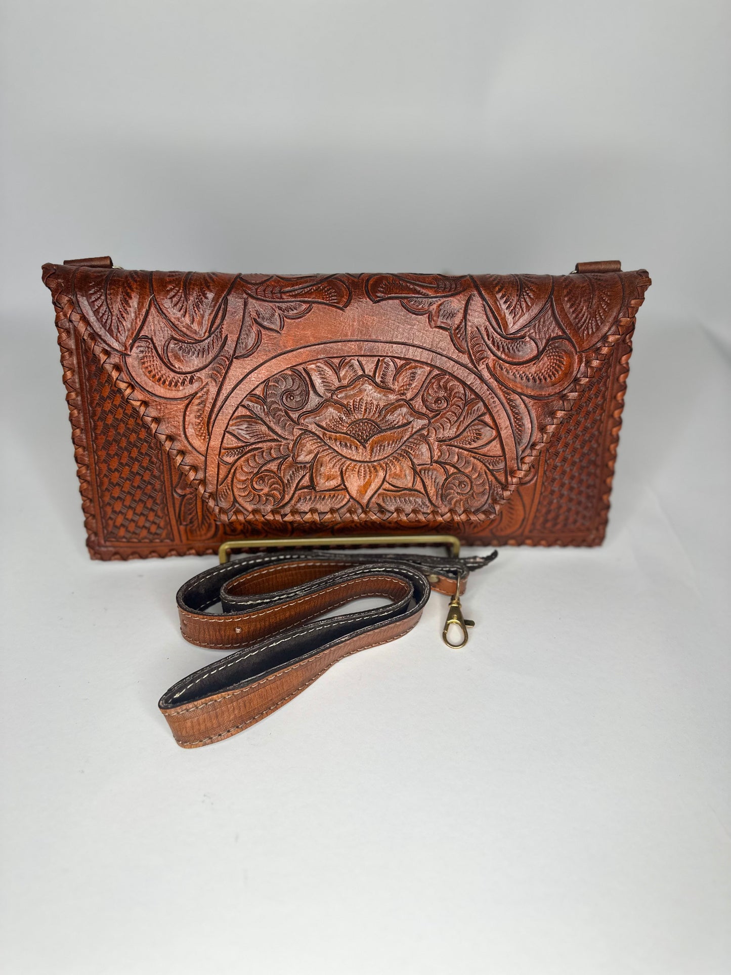 Handmade Mexican authentic leather clutch with floral design etched on top flap. Squared design etched on bottom half. Color wine red with strap in front. 