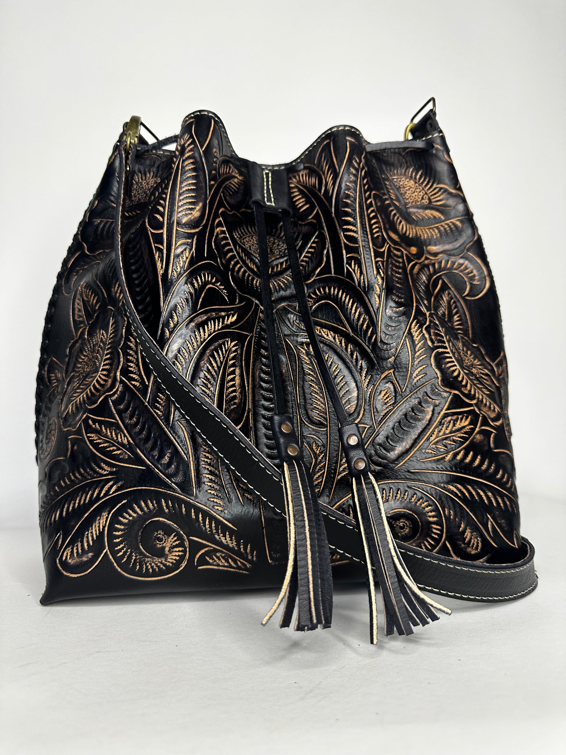 Mexican leather backpack with contrasting hand etched design throughout bag. Has one strap for crossbody capability and leather ties in front to close. Color black and white. 