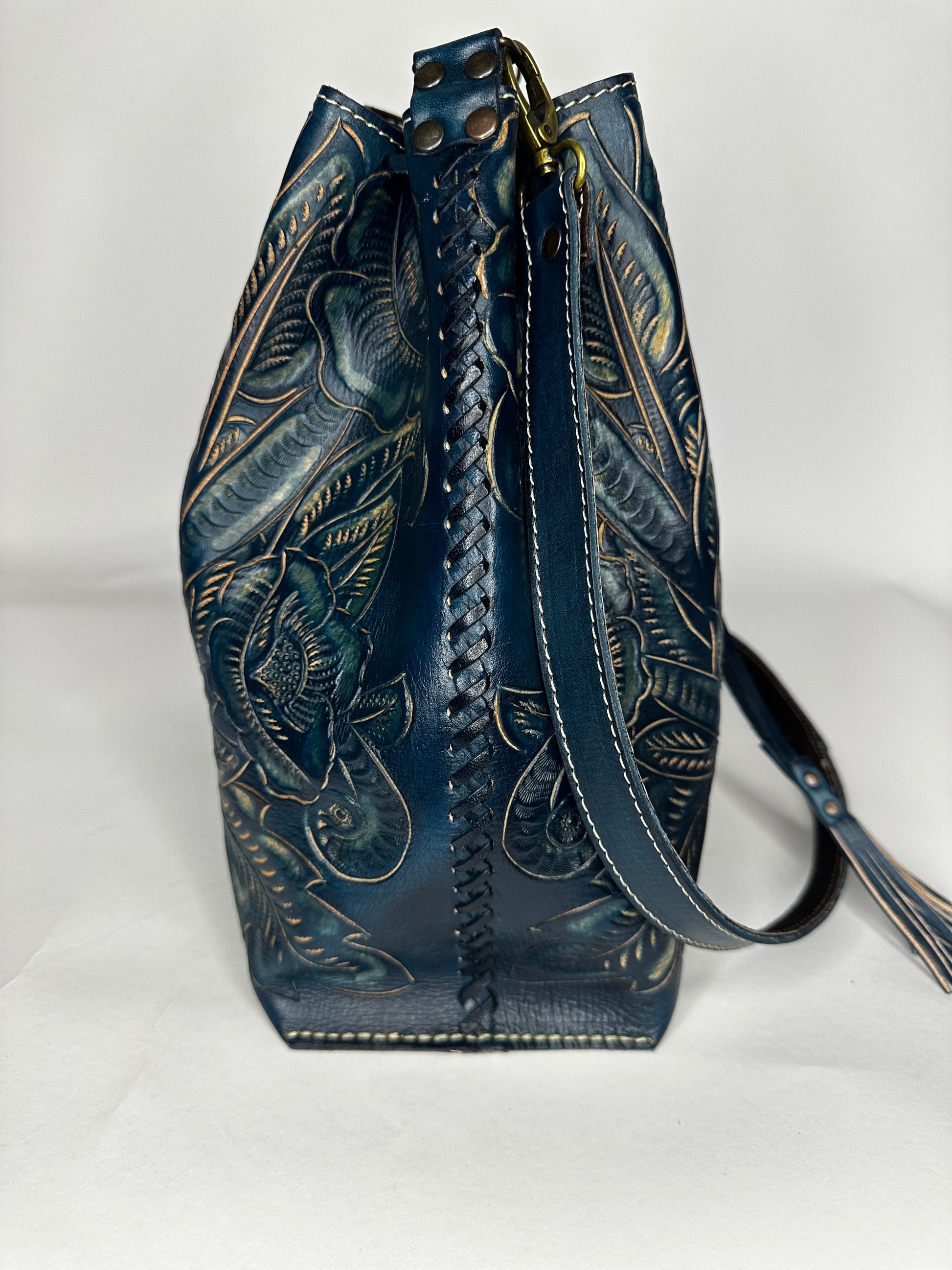 Mexican leather backpack with contrasting hand etched design throughout bag. Has one strap for crossbody capability and leather ties in front to close. Leather stitching on the side. 