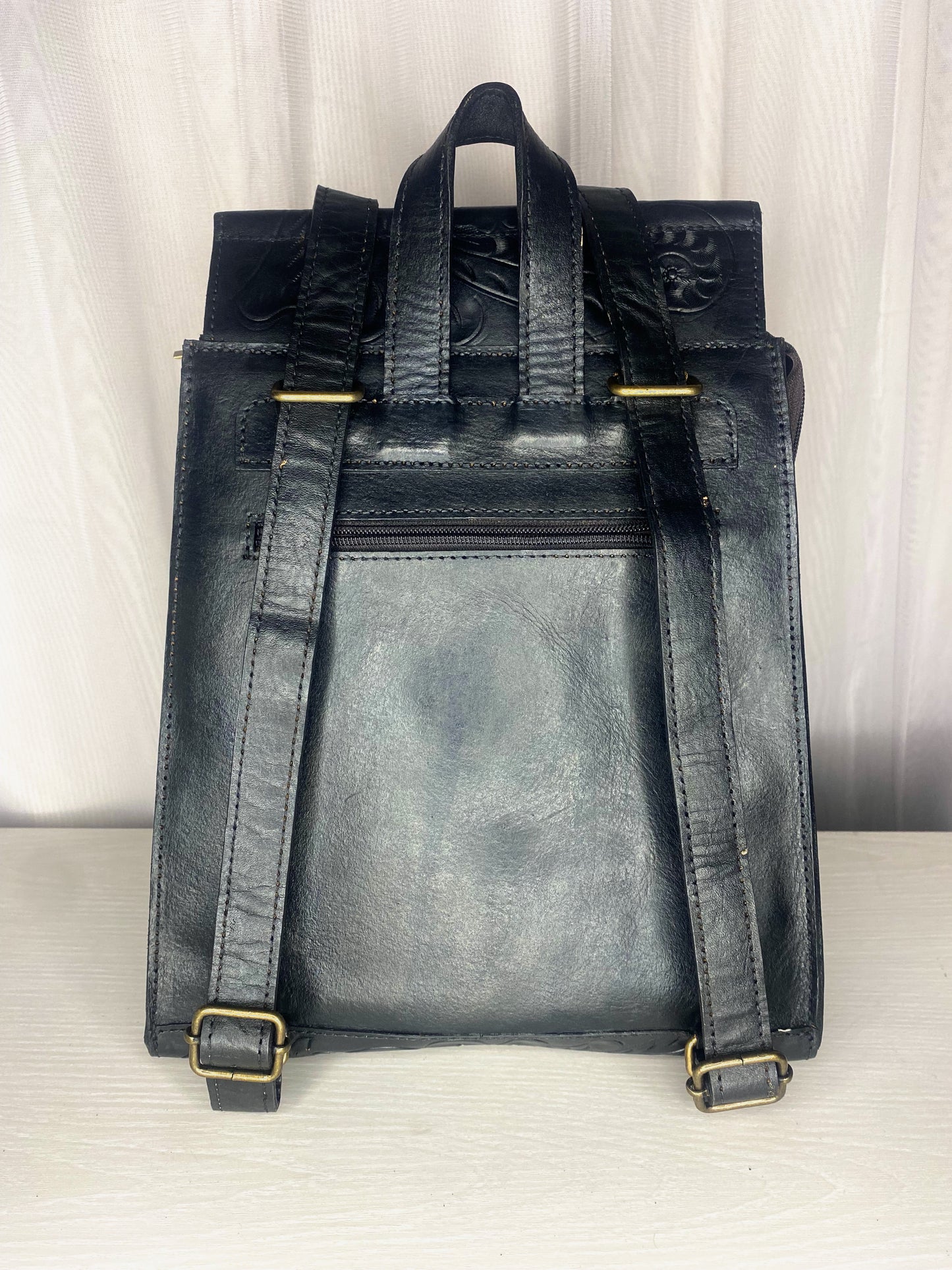 Medium sized authentic leather backpack. Trapezoid shaped with flap with Mexican design on the flap. Straps can be converted to crossbody or used as dual straps.  Back view of straps in color black. 
