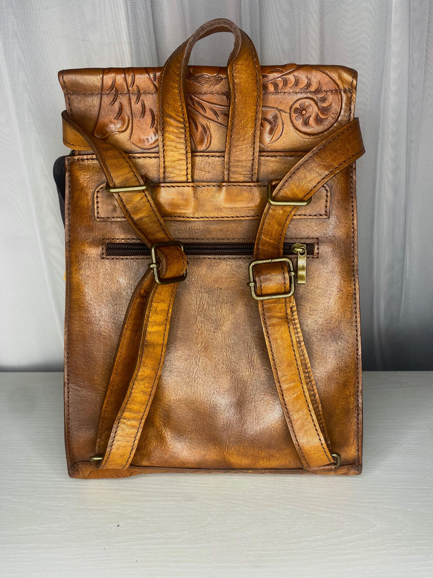 Medium sized authentic leather backpack. Trapezoid shaped with flap with Mexican design on the flap. Straps can be converted to crossbody or used as dual straps.  Back view of straps in color brown.