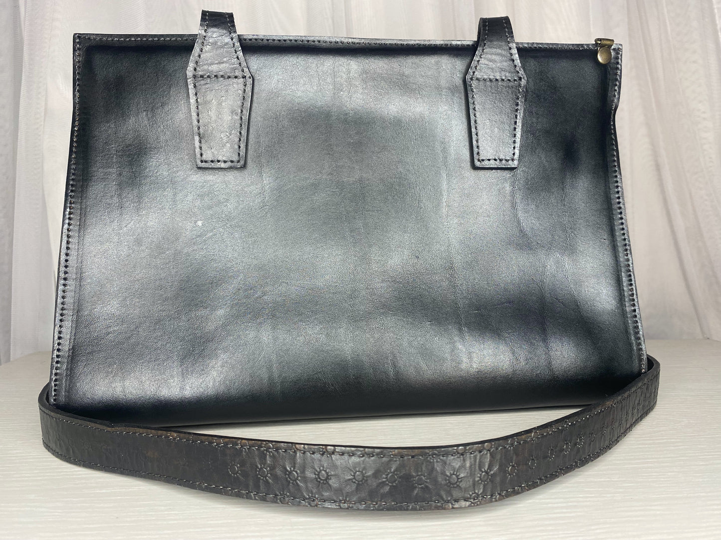 large sized leather tote bag with strap attachment for crossbody ability. Mexican etched design on ends of the tote.  Front view in color black with strap. 